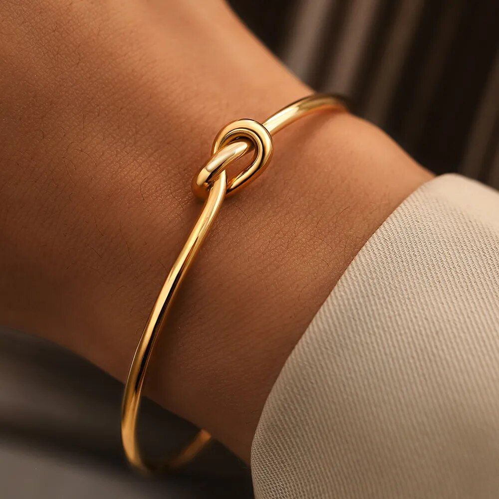 A close-up of a Twist Knot Stainless Steel Cuff Bracelet on a person's wrist, highlighting the latest in fashion trends, against a blurred beige background.