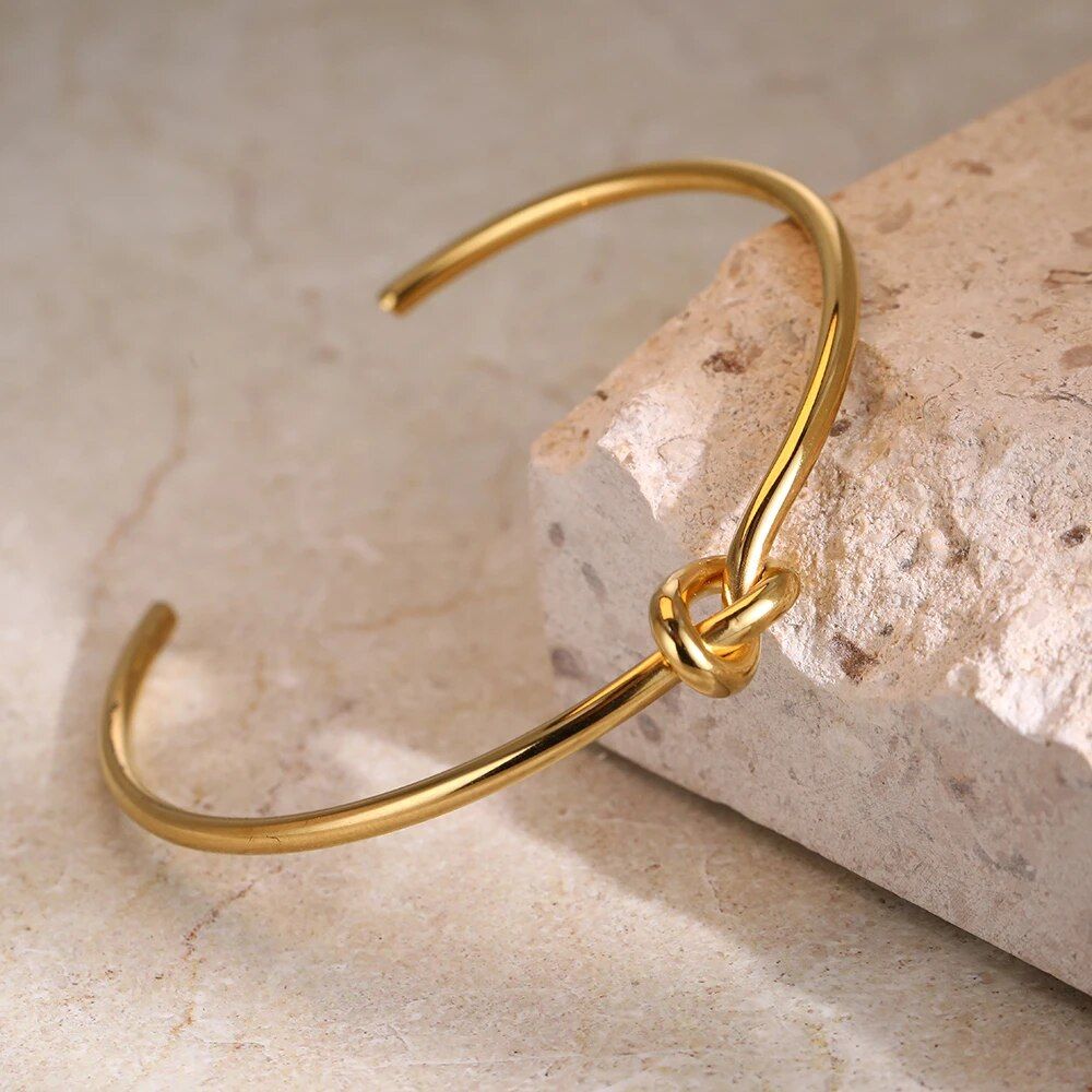 A Twist Knot stainless steel cuff bracelet rests on a stone surface, showcasing an elegant design with a focus on minimalistic luxury in line with new fashion trends.