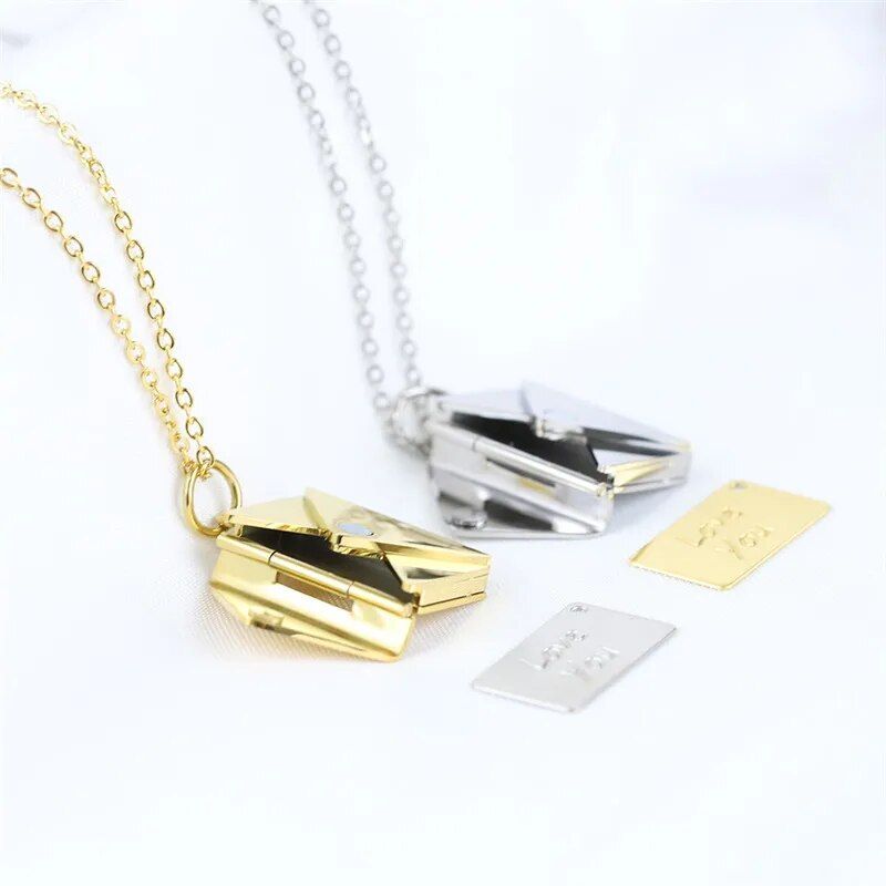 Love Letter Envelope pendant necklaces shaped like paper airplanes, accompanied by matching metallic tags, on a white background, representing new fashion trends.