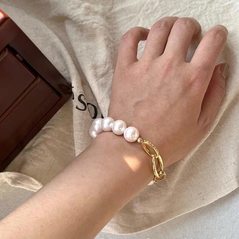 A close-up of a hand sporting a Chic Crystal & Pearl Hand Catenary Fashion Mood Tracker Bracelet paired with a gold chain bracelet, resting on a linen fabric with a brown leather fashion accessory nearby.