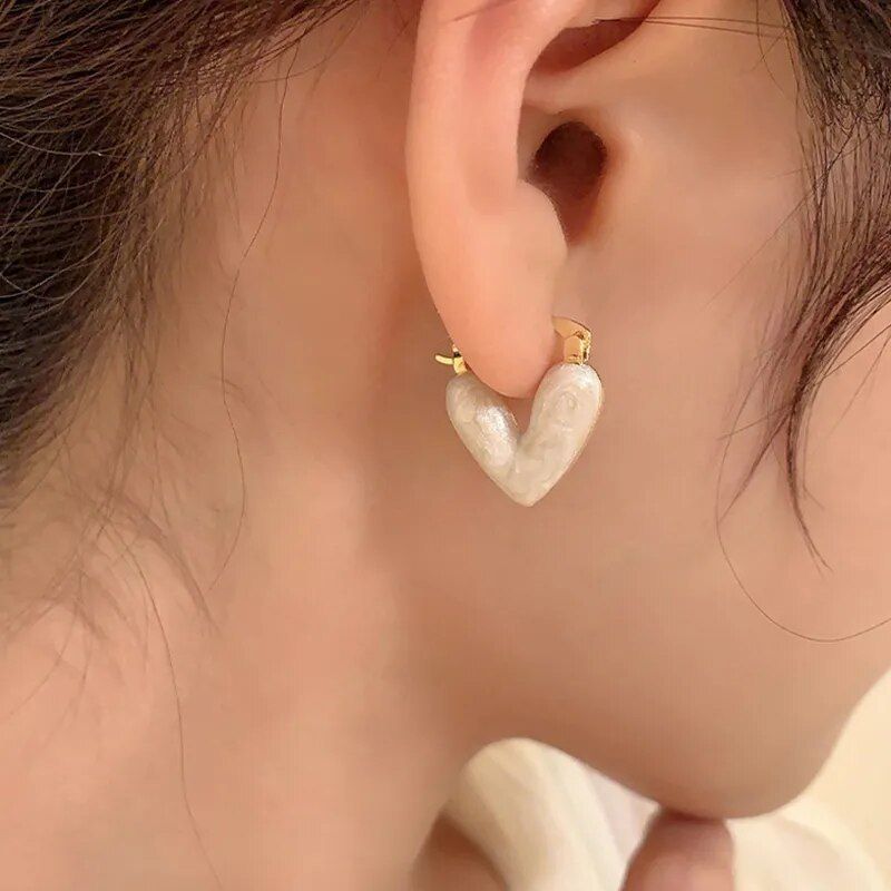 A close-up of a woman's ear wearing Elegant Heart Small Drop Earrings for Women, with a marble-like texture, representing the latest fashion trends.