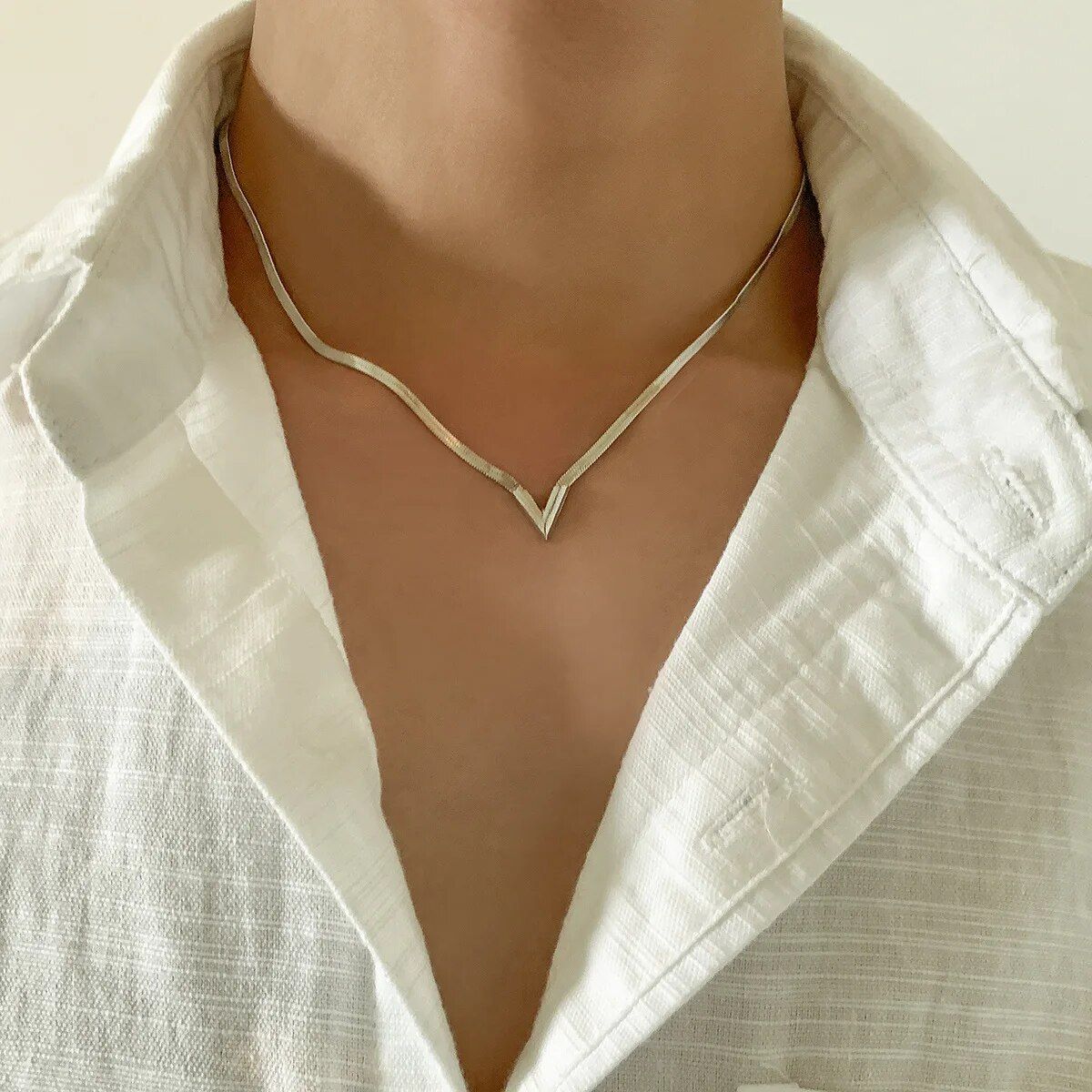 Close-up of a person wearing a white shirt with an Elegant V-Shaped Flat Snake Chain Necklace, focusing on the collar area, reflecting new fashion trends.