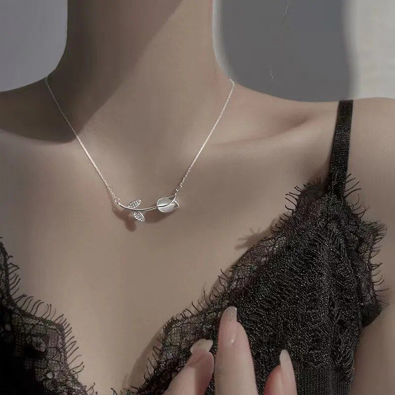 Close-up of a Classy Microinlaid Tulip Pendant Necklace on a woman wearing a black lace dress, with her hand adjusting the necklace.