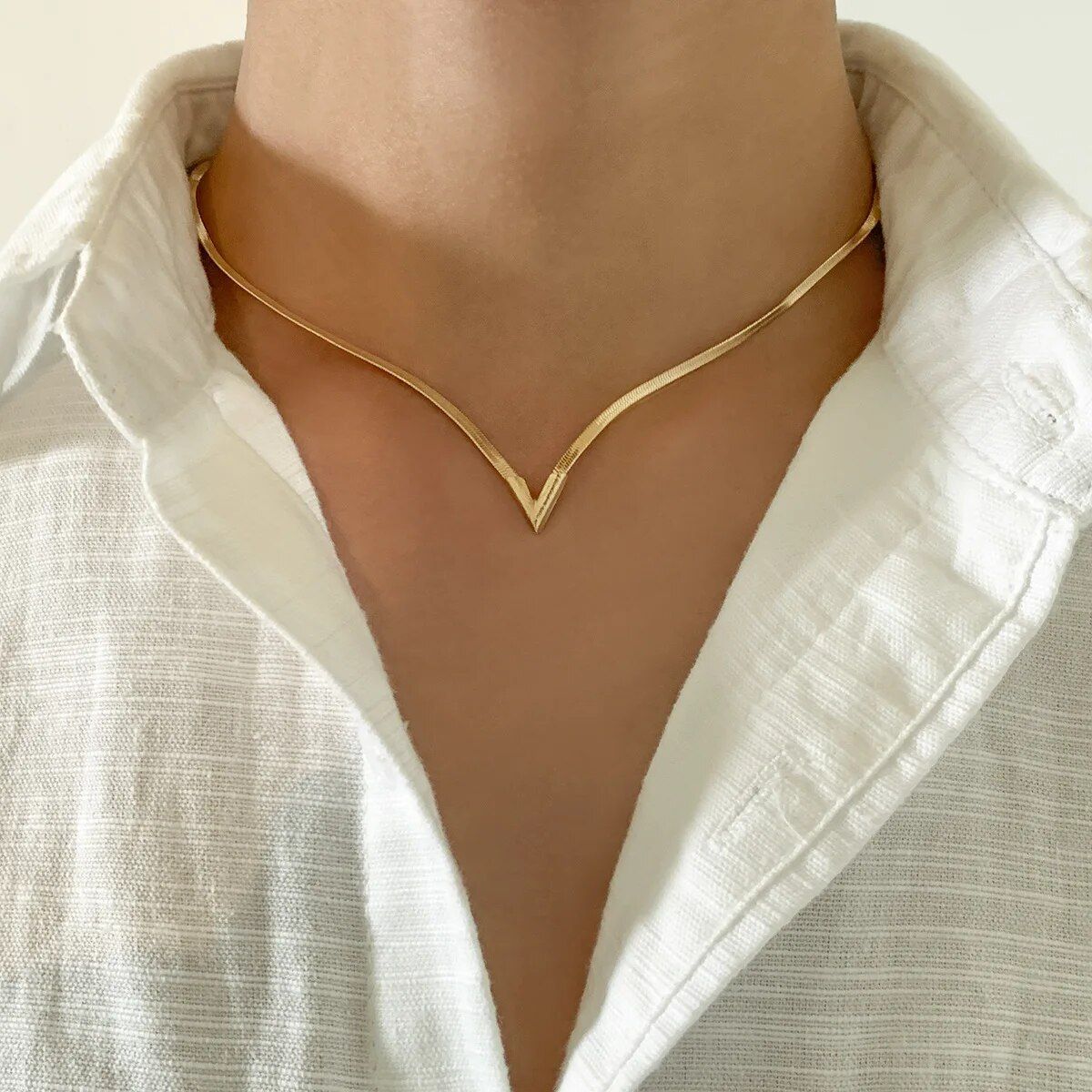 A person wearing a white shirt and an Elegant V-Shaped Flat Snake Chain Necklace, a key fashion accessory, against a light background.