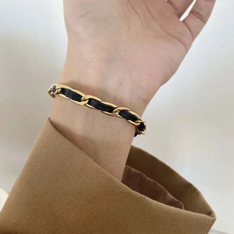 A person's wrist adorned with an Elegant Vintage Rose Gold Black Woven Bracelet, embodying current fashion trends, contrasted against a beige sleeve.