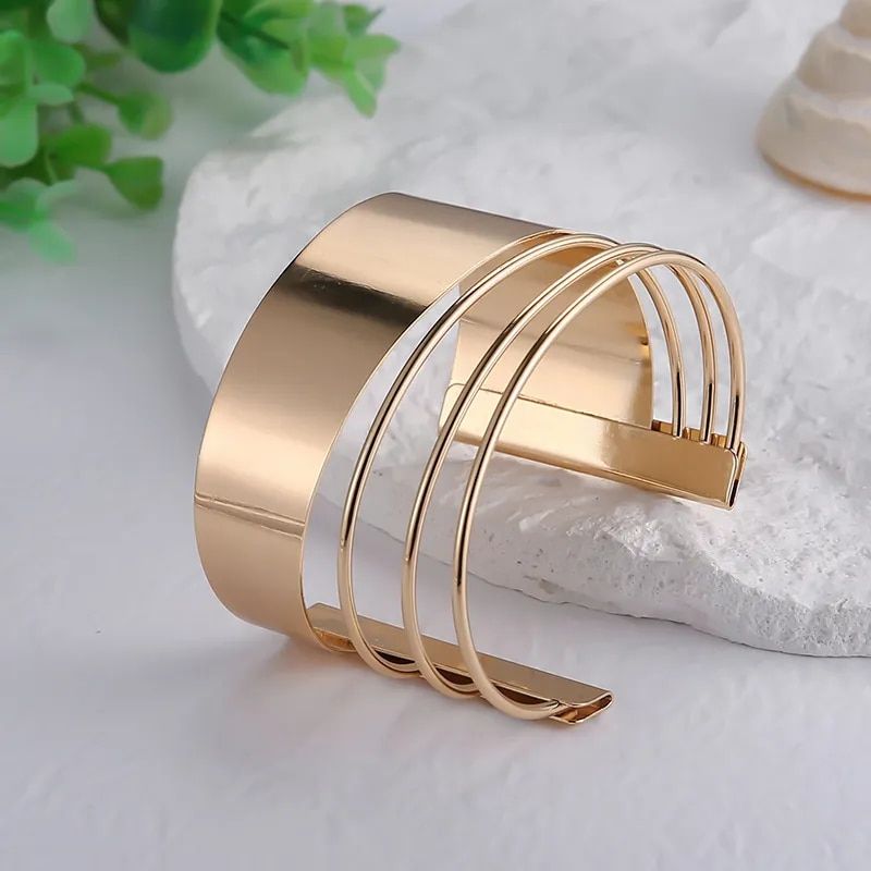 Women's Bohemian Gold-Plated Geometric Cuff Bangle with a sleek, wide band and an open-ended thin strips design, displayed on a light-colored surface. This piece embodies the latest fashion trends.