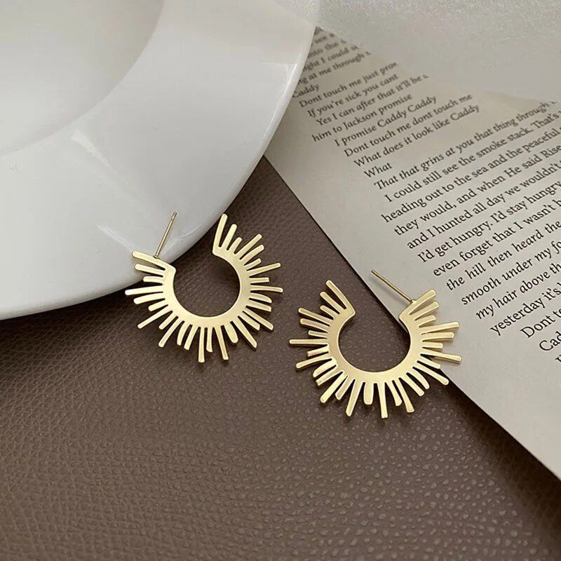 Chic Sunflower Hoop Earrings for Women, exemplifying current fashion trends, placed on a brown surface next to an open book and a white ceramic bowl.