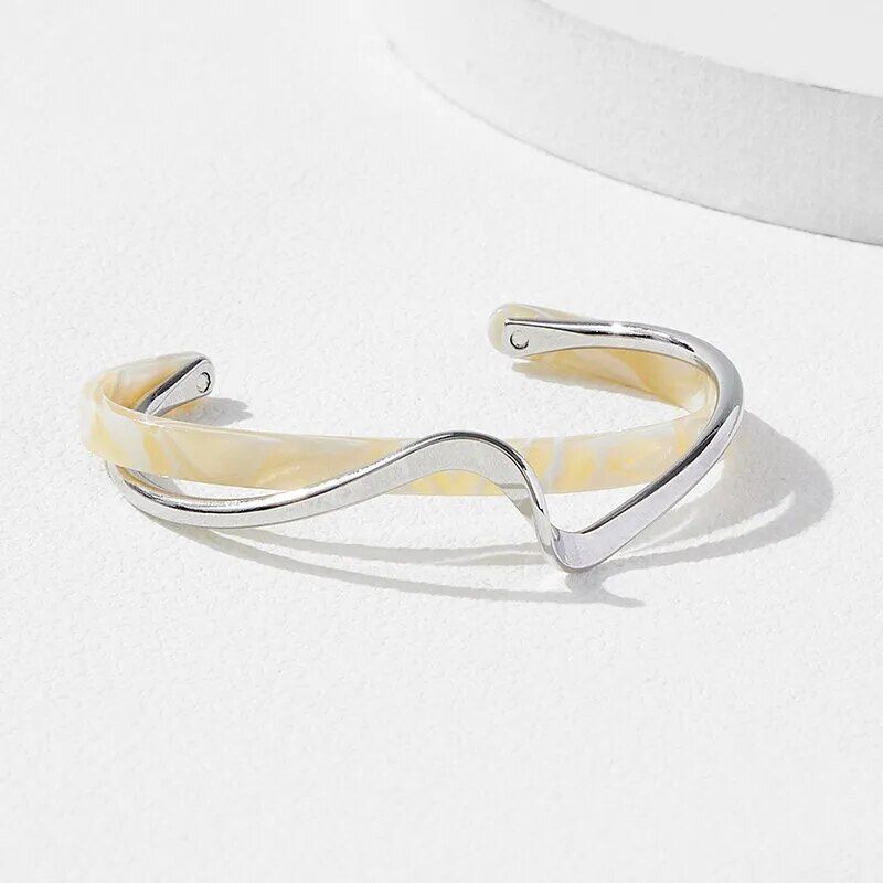 Geometric metal charm bracelet for women with creamy yellow accents, displayed on a white surface with a shadow to the right, embodying a chic fashion accessory.