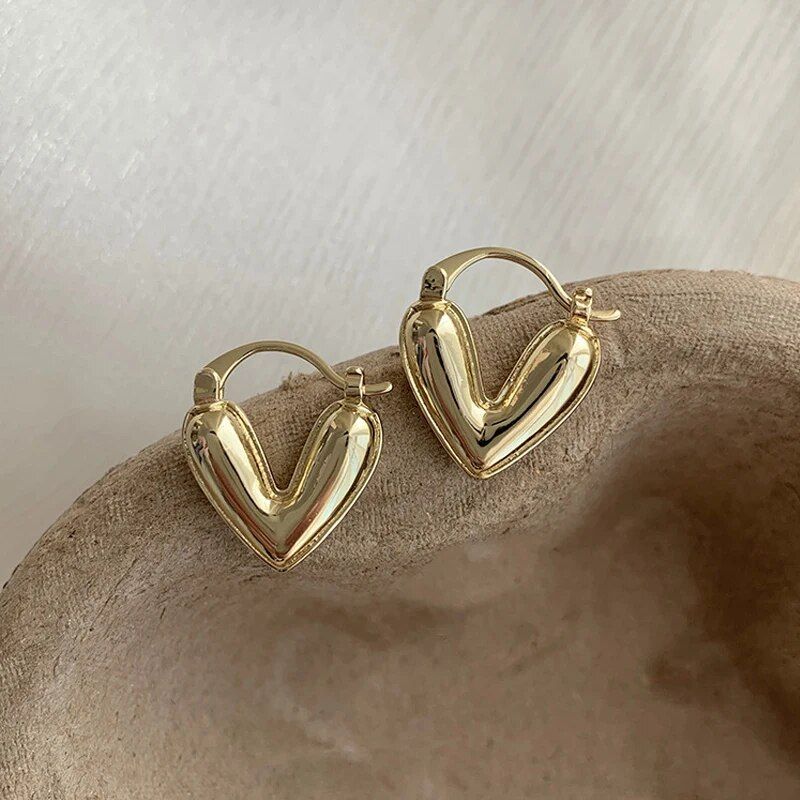 A pair of Elegant Heart Small Drop Earrings for Women, exemplifying the latest fashion style, resting on a beige textured surface.