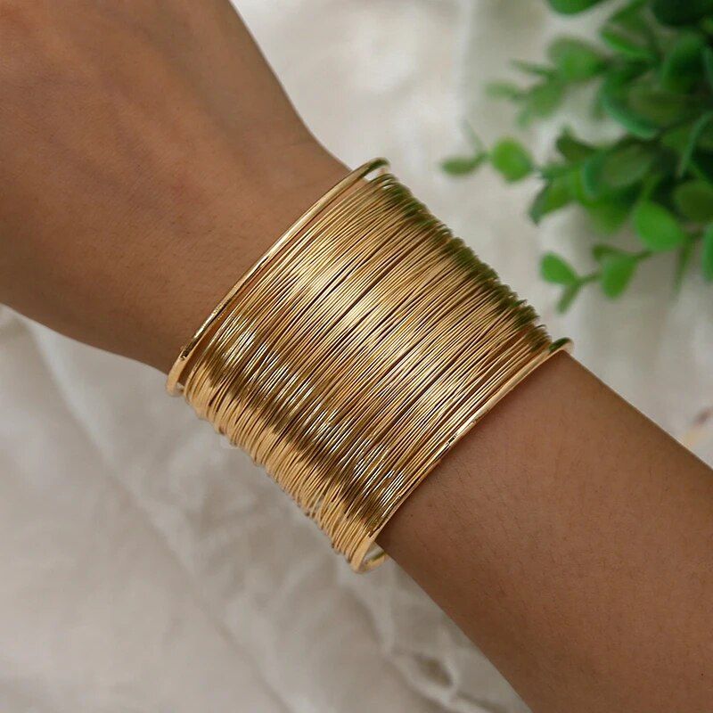 A close-up of a wrist adorned with a Women's Bohemian Gold-Plated Geometric Cuff Bangle, showcasing new fashion trends against a light fabric background.