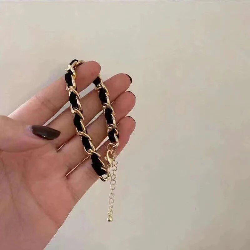 A hand with brown nail polish holds an Elegant Vintage Rose Gold Black Woven Bracelet against a pale background, showcasing the latest in women's fashion style.