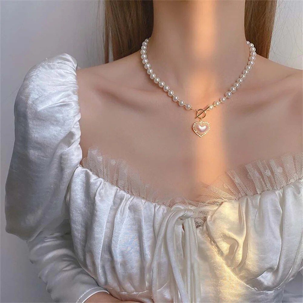 Woman wearing a Vintage Heart Pendant Pearl Necklace, and an off-shoulder white blouse with lace details as part of the latest womens fashion.