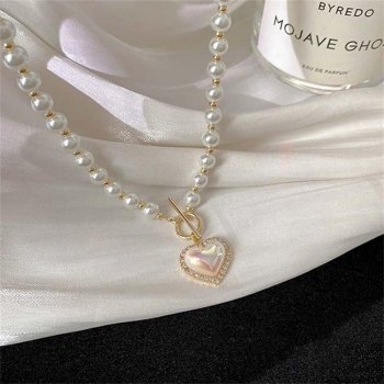 Vintage Heart Pendant Pearl Necklace with a heart-shaped pendant on a white fabric, next to a Byredo Mojave Ghost perfume bottle, epitomizing elegant women's fashion.