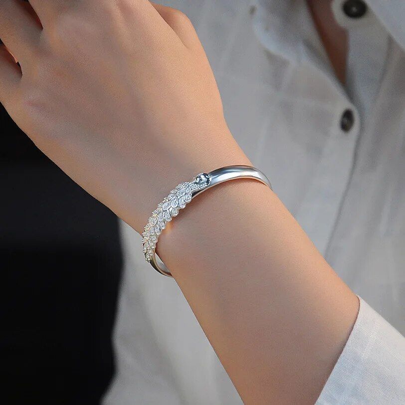 A close-up of a woman's wrist wearing a Women's Vintage Peacock Cuff Bracelet - Antique Silver Plated with an intricate design. She is dressed in a white shirt showcasing the latest women's fashion.