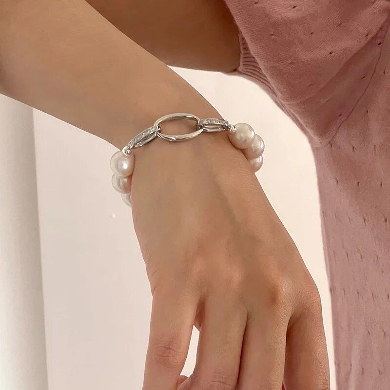 A person wearing a Chic Crystal & Pearl Hand Catenary Fashion Mood Tracker Bracelet on their wrist against a pink wall showcases the latest fashion accessory.