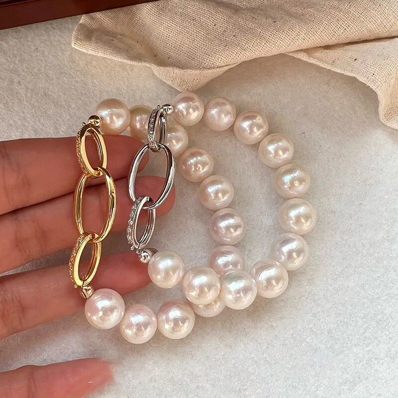 A hand showcasing two Chic Crystal & Pearl Hand Catenary Fashion Mood Tracker Bracelets embodying new fashion, one with large pearls and another featuring gold and silver interlocked rings, set against a neutral fabric background.