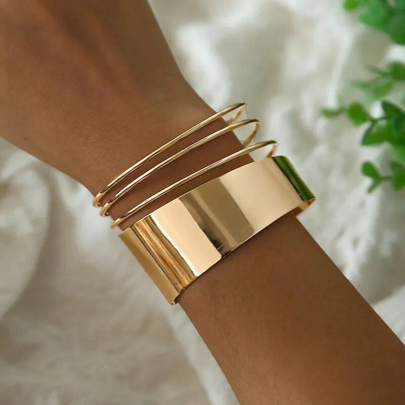 A close-up image of a wrist adorned with the Women's Bohemian Gold-Plated Geometric Cuff Bangle, featuring a wide cuff and slender bangles, against a soft, white fabric backdrop captures the essence of new fashion style.