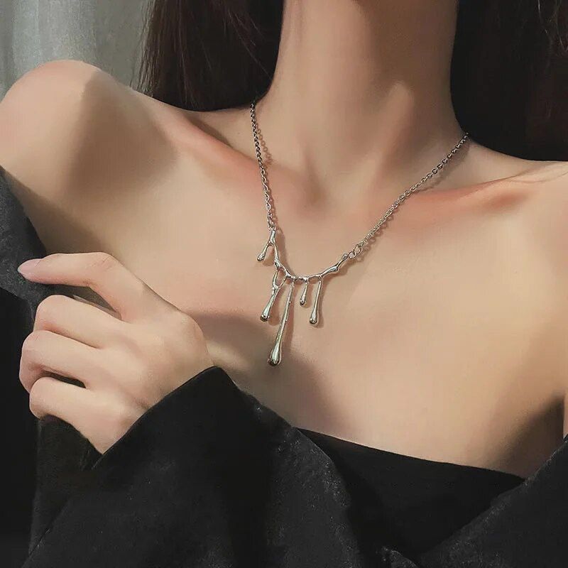 Woman wearing a black top and a Elegant Liquid Drop Shape Yarn Pendant Necklace with elongated pendant links, lightly holding her collarbone. This stylish ensemble showcases the latest fashion trends.