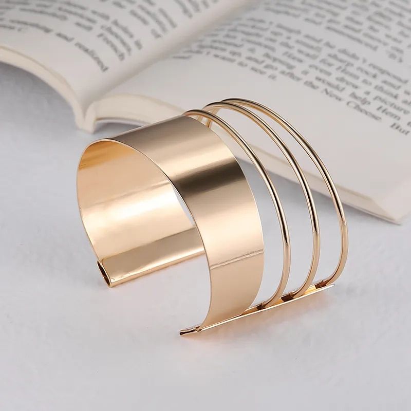 A Women's Bohemian Gold-Plated Geometric Cuff Bangle with multiple thin bands, displayed against a book backdrop on a white surface, embodying new fashion trends.