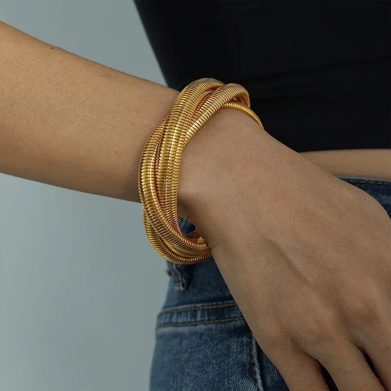 A person's wrist adorned with multiple Trendy Punk Style Gold-Plated Geometric Womens Bangles, reflecting new fashion trends, set against a grey background.