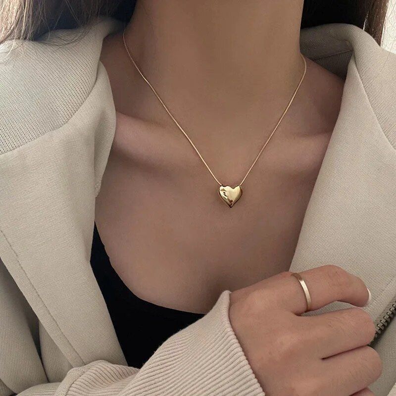 Close-up of a woman wearing a Gothic Trendy Heart pendant necklace and a white ring, set against a black top and cream blazer as part of the latest women's fashion trends.