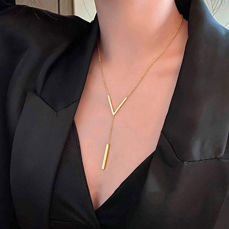 Close-up of a woman wearing a Gold-Toned V-Shaped Clavicle Womens Necklace with a long pendant, accessorized with a sleek black blazer, embodying current fashion trends.