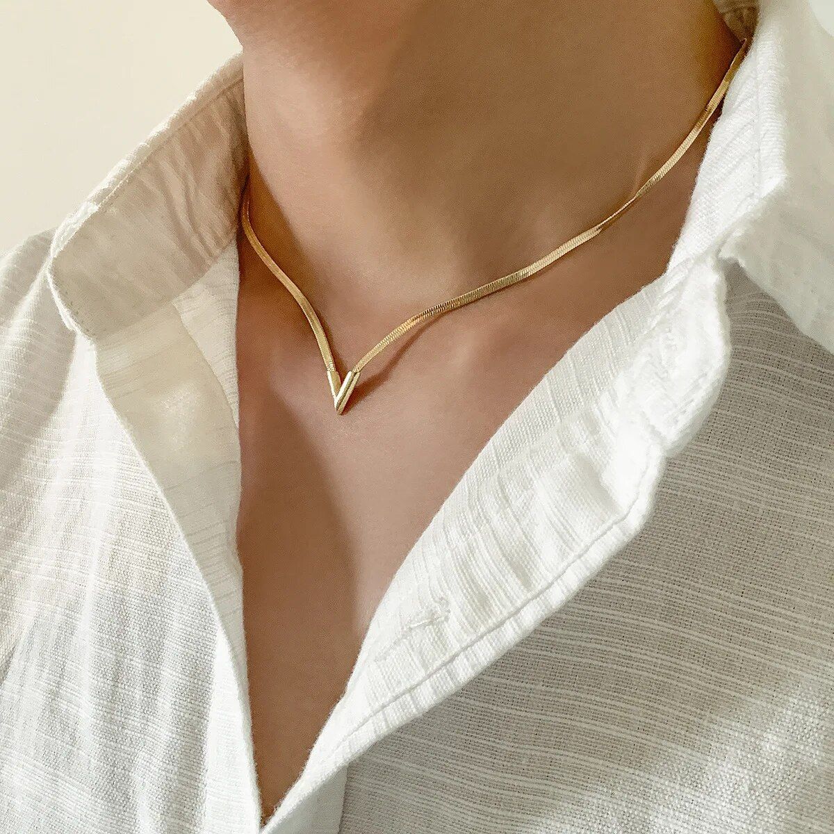 Close-up of a person wearing an Elegant V-Shaped Flat Snake Chain Necklace, showcasing the latest fashion trend, over an open white shirt collar.