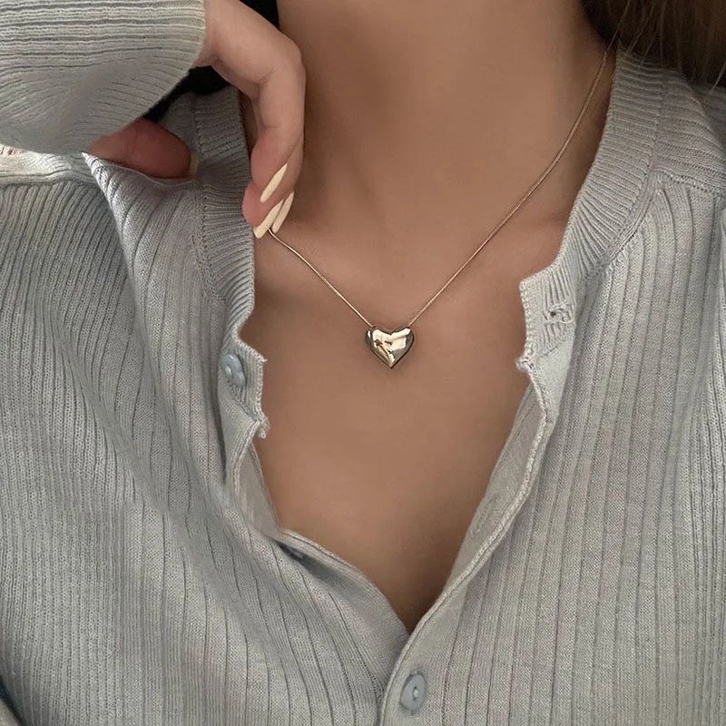 Close-up of a woman wearing a gray buttoned shirt and a Gothic Trendy Heart Pendant Necklace, focusing on the necklace and part of her collar, capturing elements of current fashion trends.