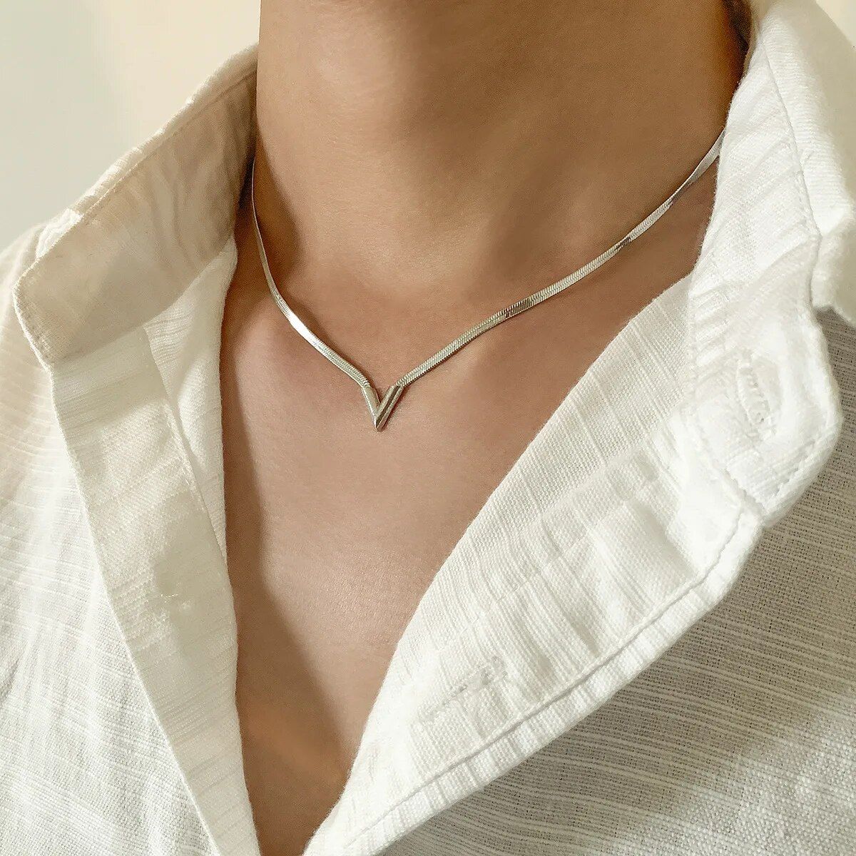 A close-up of a person wearing a stylish Elegant V-Shaped Flat Snake Chain Necklace over a white blouse, following new fashion trends at the neckline area.