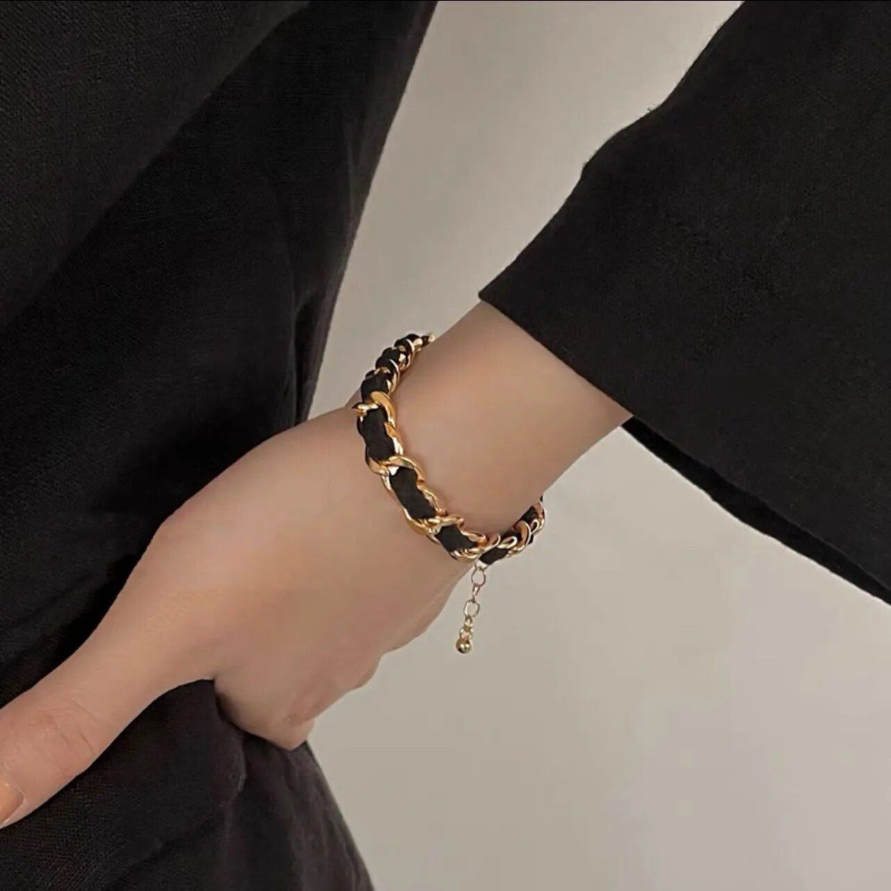 A person wearing an Elegant Vintage Rose Gold Black Woven Bracelet on their wrist against a backdrop of dark clothing, embodying the latest fashion trends.
