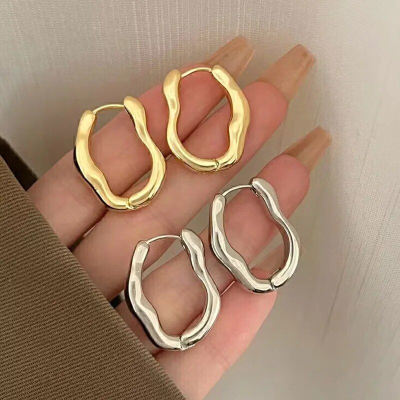 A person holding four Luxurious Geometric Hoop Earrings for Women, two gold and two silver, representing a new fashion style in their palm.