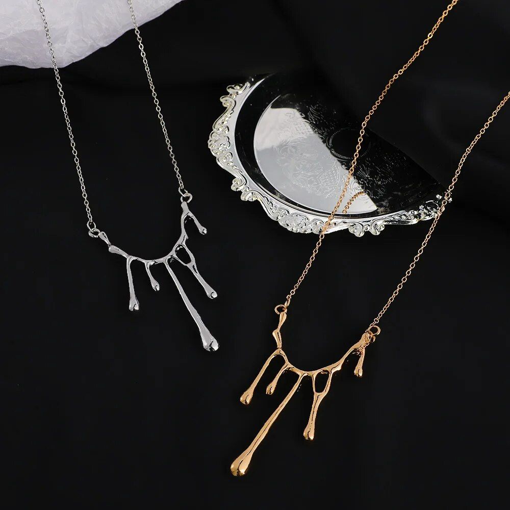 Two Elegant Liquid Drop Shape Yarn Pendant Necklaces in silver and gold, displayed on a reflective surface next to a white fabric, epitomizing the latest fashion trends.