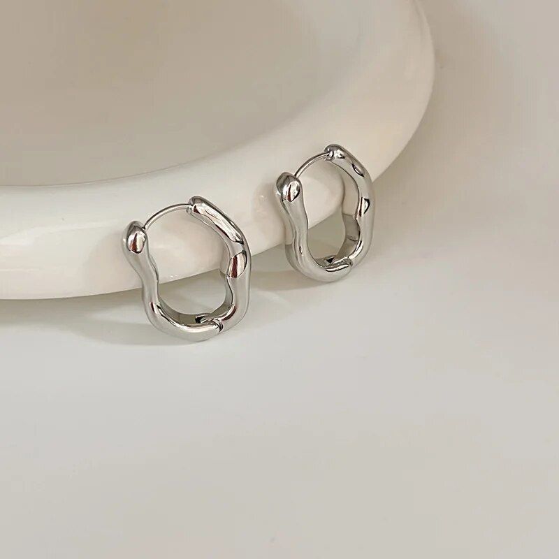 Two Luxurious Geometric Hoop Earrings for Women with a new fashion, open-circle design, displayed against a cream, curved backdrop.