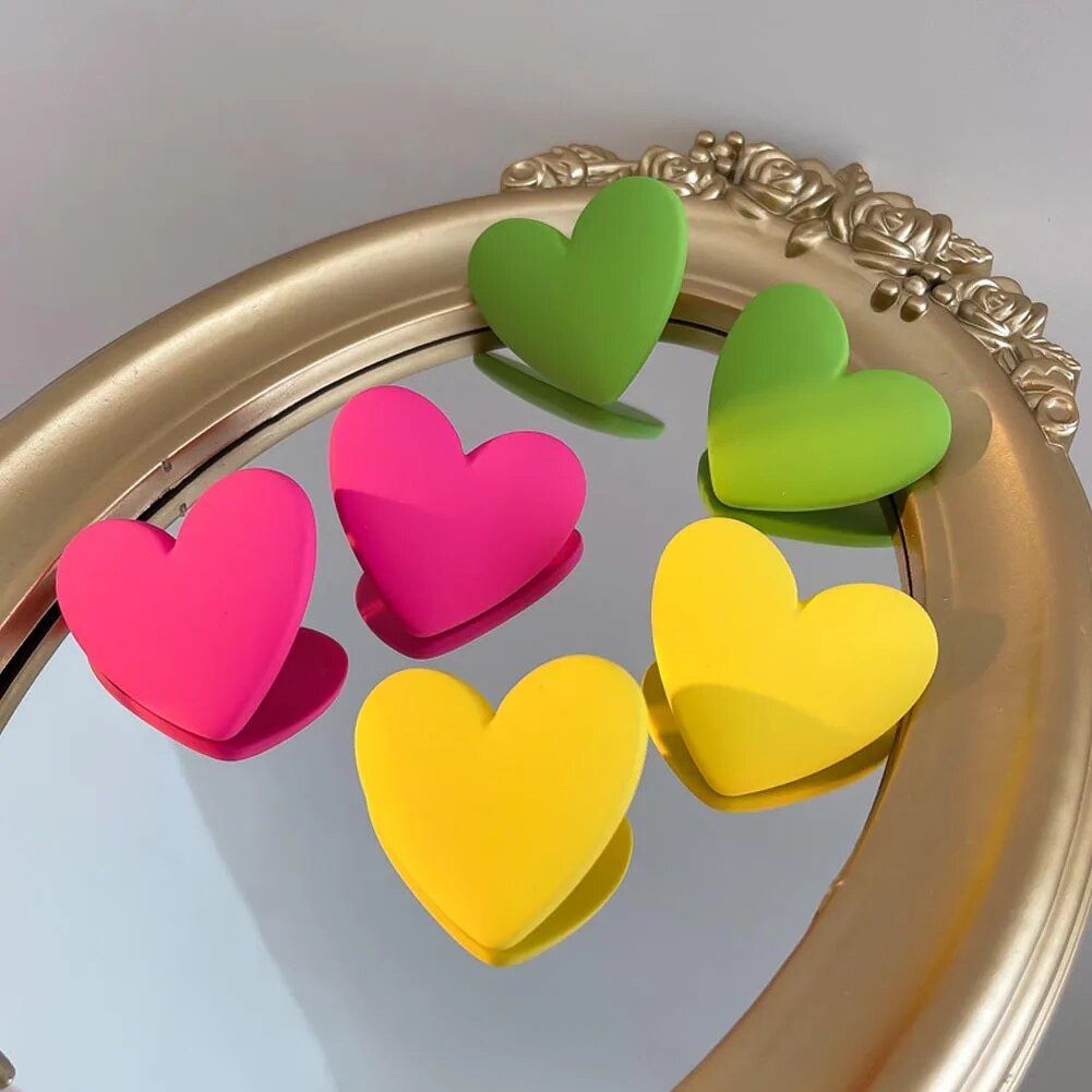 Five Colorful Heart-Shaped Acrylic Earrings for Women (pink, green, and yellow) arranged on a golden-framed mirror with ornate details, reflecting the latest fashion trends.