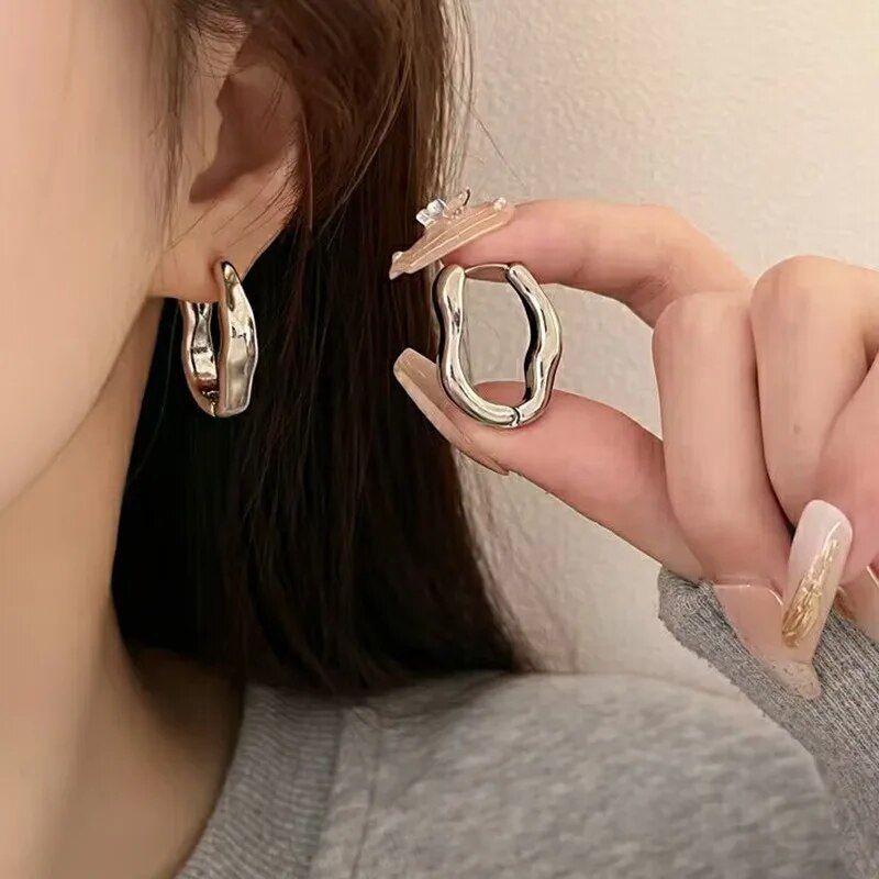A woman's hand displaying a silver abstract ring, with Luxurious Geometric Hoop Earrings worn on her visible ear, showcasing new fashion.