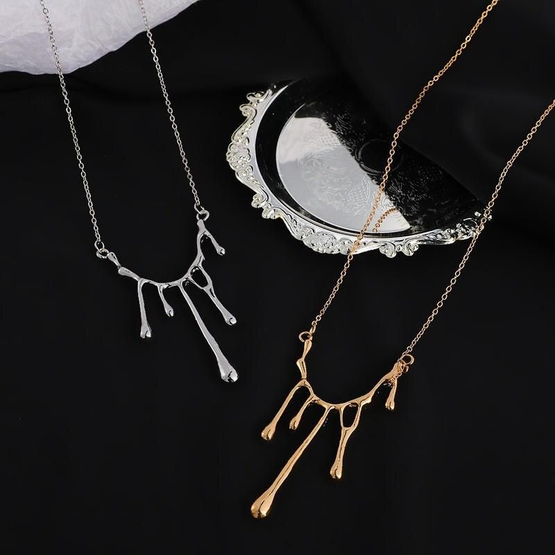 Two Elegant Liquid Drop Shape Yarn Pendant Necklaces, one silver and one gold, displayed on a black surface beside a decorative mirror. These pieces are the latest in new fashion trends.