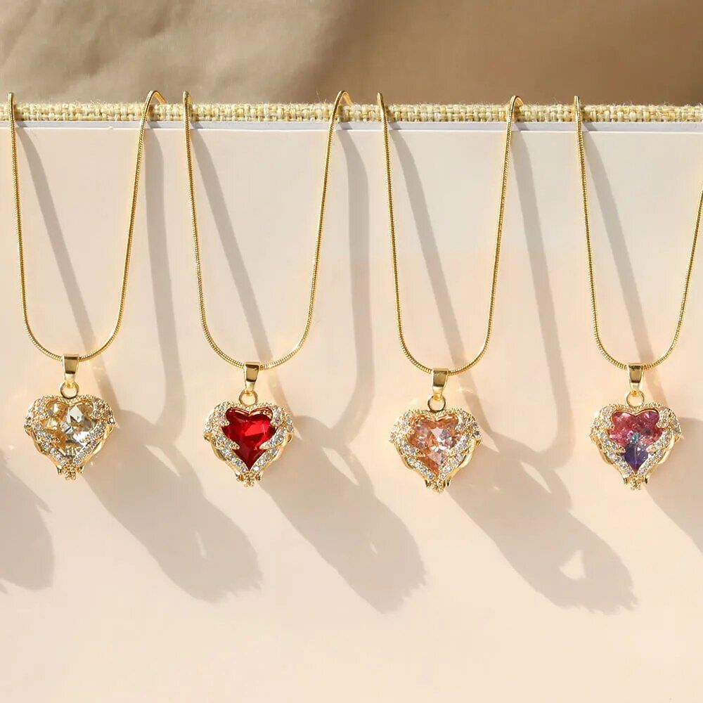Five gold-plated enamel red heart pendant necklaces with various gemstone inlays, epitomizing women's fashion style, hanging against a beige backdrop.