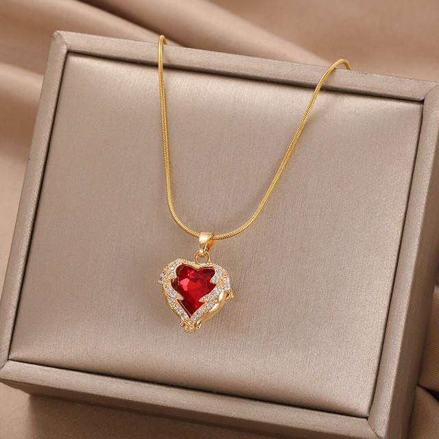 A Gold-Plated Enamel Red Heart Pendant Necklace with a large red gemstone, surrounded by smaller clear crystals, displayed in a gray box on a satin background, embodying new fashion trends.