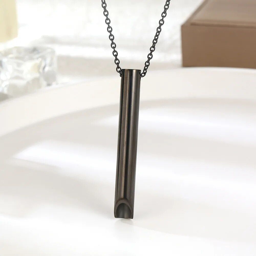 A cylindrical Stress Relief Breathing Necklace hanging from a black chain, embodying the new fashion trends, displayed above a white surface.