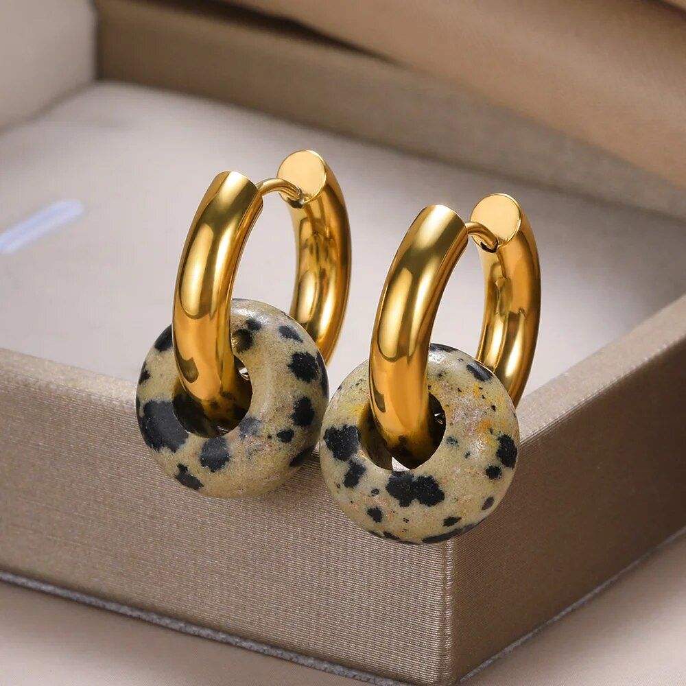 A pair of Women's Natural Stone Hoop Earrings with leopard print charms displayed on a plush beige surface, representing the latest fashion trends.